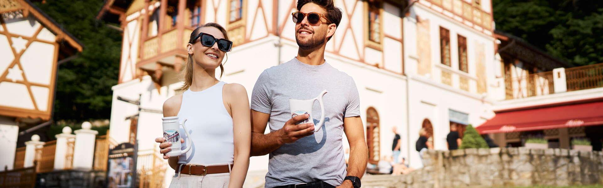 A man and a woman are smiling while strolling around the town. Szczawnica buildings in the background.